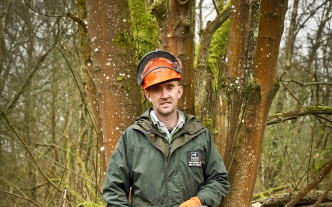 Adam stands with a chainsaw in a wood