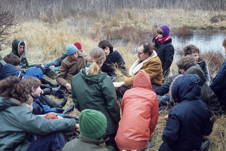 Brian Tear sitting down by a pond and surrounded by a group of children